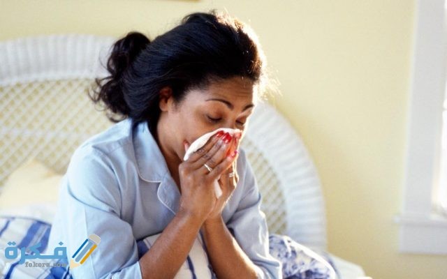 كيفية علاج انسداد الأنف بالاعشاب a woman sat in bed and blowing her nose because she has the flu